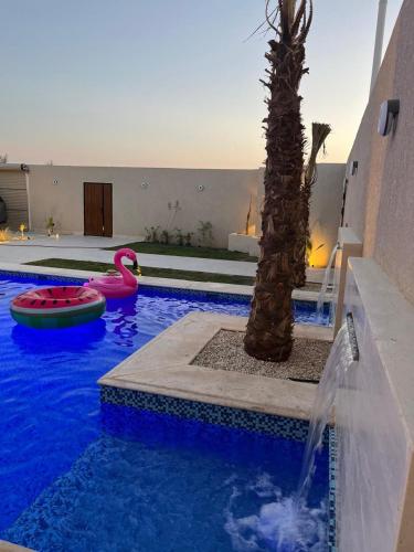 a pool with a palm tree and two inflatablelatable boats at شاليهات رزانه الفندقية in Ilbaras
