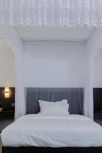 a bedroom with a white bed with white curtains at UCHA Hotel & Suites in Kampala