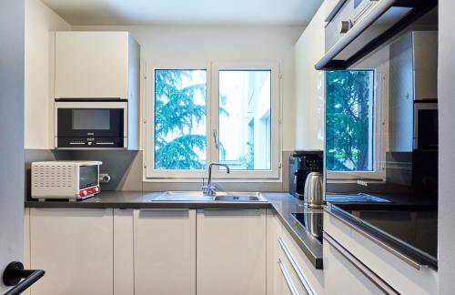 - une cuisine avec des placards blancs, un évier et 2 fenêtres dans l'établissement Beautiful central apartment near Eiffel Tower and Invalides, à Paris