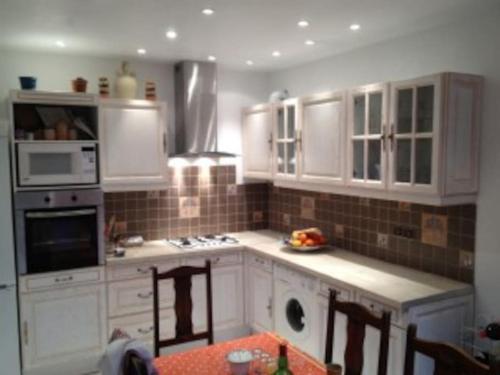 une cuisine avec des armoires blanches et une table avec des chaises dans l'établissement Maison AUBECALINIERE, à Chandolas