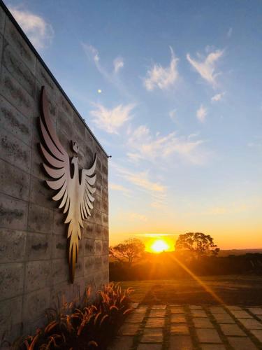 a stone wall with an eagle sign with the sunset in the background at Vinícola e Hospedaria Bonventi Ltda in Espirito Santo Do Pinhal