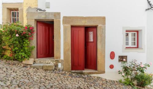 two red doors on a white building with flowers at Casas Miguel Bombarda in Castelo de Vide