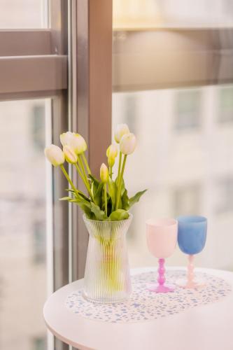 a vase with flowers on a table with two glasses at 코아루 시티 in Yeosu