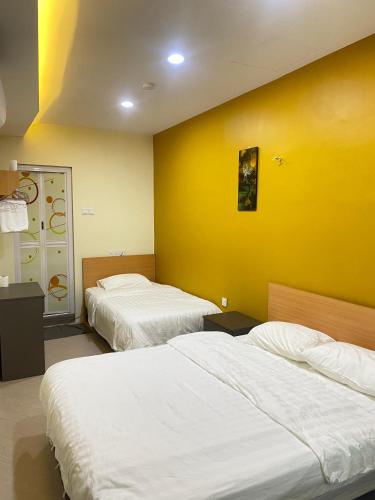 two beds in a room with a yellow wall at Sunshine Hotel in Bahau