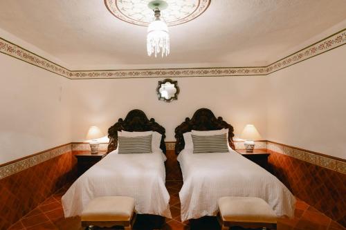 two beds in a room with two chairs and a chandelier at Hotel Hacienda La Cieneguita in San Miguel de Allende
