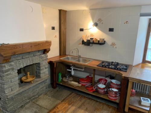 a kitchen with a stone fireplace and a sink at Lu Biulè Ca' d'Aldo in Groscavallo