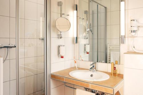 ein Bad mit einem Waschbecken und einer Dusche mit einem Spiegel in der Unterkunft Luckai Hotel & Restaurant Inhaber Dennis Burmann in Freienohl