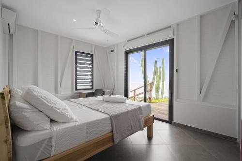 a white bedroom with a bed and a balcony at Villa Kimloa in Case-Pilote