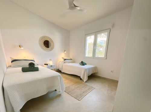 a white bedroom with two beds and a window at Casa Palmerita a 7 minutos andando de una playa de aguas cristalinas in Teulada