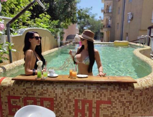two women sitting at a table near a swimming pool at Хотел ЮГ in Primorsko
