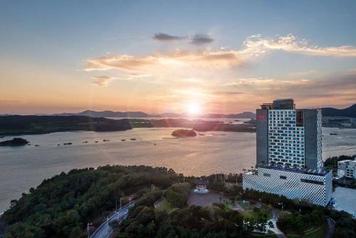 a large building next to a river with the sunset at Ramada Plaza by Wyndham Dolsan Yeosu in Yeosu