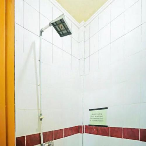 a bathroom with a light on a white tiled wall at Wisma Pinggir Mitra RedDoorz in Tanjung Pinang 