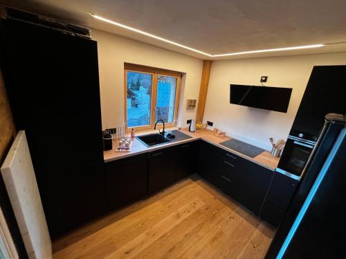 d'une cuisine avec des placards noirs, un évier et une fenêtre. dans l'établissement Le Chappart, aux Carroz d'Arâches