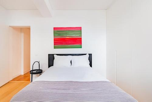a bedroom with a white bed with a painting on the wall at Oeiras Spacious and Coastal Flat in Paço de Arcos