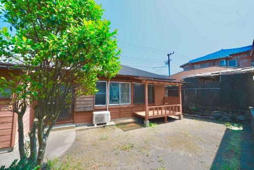 a wooden house with a porch and a tree at ペンションとみや 1組限定 in Oshima