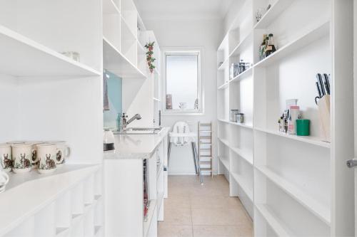 a white kitchen with white shelves and a sink at Spyglass Mollymook in Mollymook