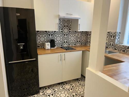 une cuisine avec des armoires blanches et un réfrigérateur noir dans l'établissement Appartement magnifique paris 18, à Paris