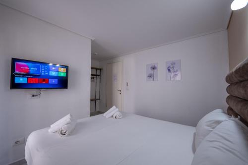 a white bedroom with a bed with a tv on the wall at Hotel Elite Sarande in Sarandë