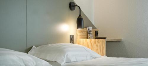 a bed with white sheets and a lamp next to it at Brit Hotel Essentiel Arverne - Clermont-Ferrand Sud in Aubière