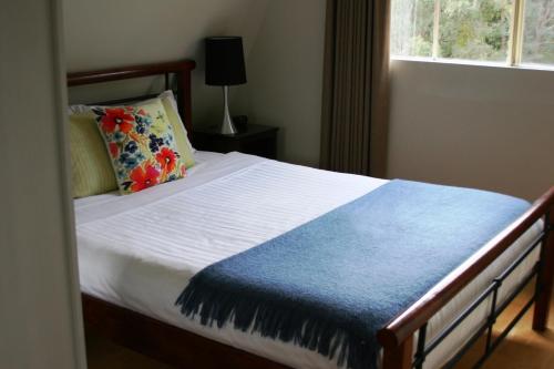 a bedroom with a bed with a blue blanket and a window at The Barn at Charlottes Hill in Healesville