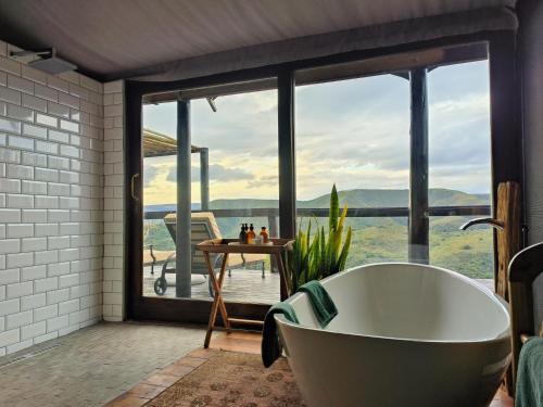 a bath tub in a bathroom with a large window at Camp Figtree by The Oyster Collection in Addo
