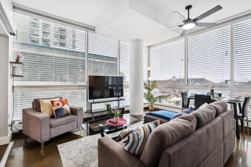 a living room with couches and a tv and large windows at Modern Condo w Balcony - Steps from Stampede Park in Calgary