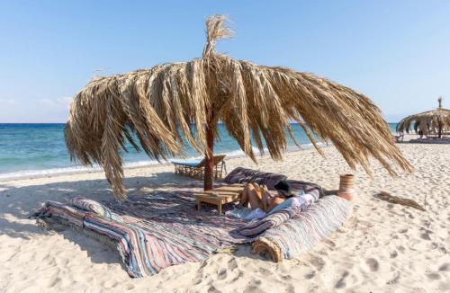 a person laying on a beach under a straw umbrella at Aqua Sun in Nuweiba