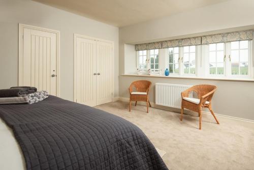 a bedroom with a bed and two chairs and windows at Farm Cottage in Berwick-Upon-Tweed