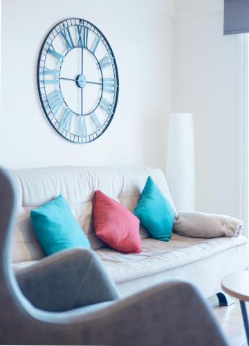 a clock on the wall above a couch with pillows at Maestro III Apartment in Larnaca