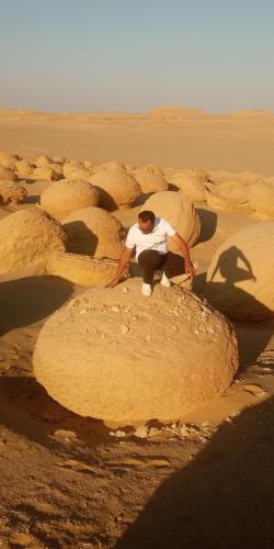 a man sitting on a rock in the desert at مخيمات وادى الريان بالفيوم in Qaryat Ḩātim aţ Ţāʼī