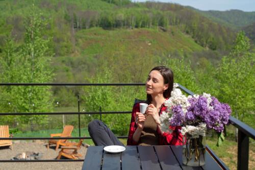 a woman sitting at a table with a cup of coffee at Dobrede - будиночки під лісом in Dubrynychi