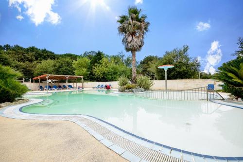 une grande piscine avec un palmier en arrière-plan dans l'établissement Mobil-home climatisé, camping 3étoiles, 5 min du Lac et à 15 min de Mimizan-Plage, à Sainte-Eulalie-en-Born
