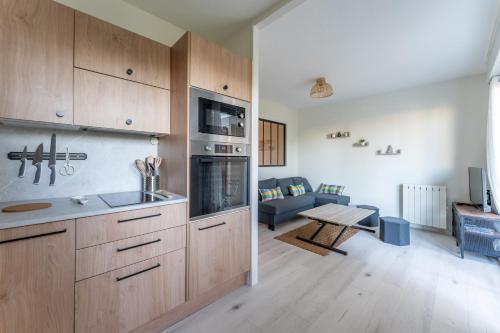 une cuisine avec des placards en bois et un salon dans l'établissement Cosy Gallieni - Bel appt avec terrasse à Merignac, à Mérignac