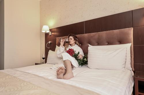 a young woman sitting on a bed drinking from a glass at Grand Hotel Coroana in Bistriţa
