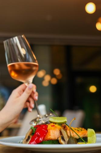 a person holding a glass of wine next to a plate of food at Grand Hotel Coroana in Bistriţa