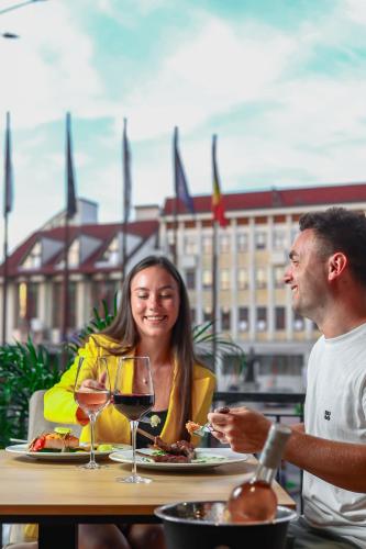 a man and a woman sitting at a table with wine glasses at Grand Hotel Coroana in Bistriţa
