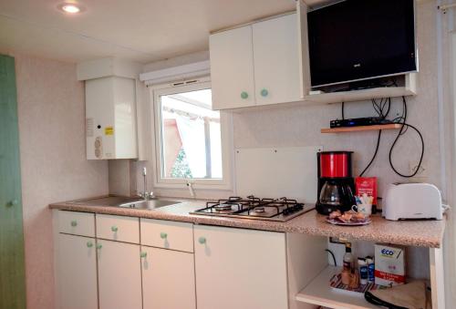 d'une cuisine avec des placards blancs, une cuisinière et une fenêtre. dans l'établissement Mobil-home climatisé, camping 3étoiles, 5 min du Lac et à 15 min de Mimizan-Plage, à Sainte-Eulalie-en-Born