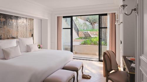 a white bedroom with a bed and a large window at Airelles Château de la Messardière in Saint-Tropez