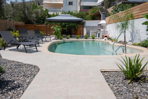 a pool in a yard with chairs and an umbrella at Centro Stone House in Tolo