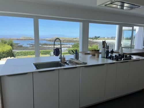une cuisine avec des placards blancs et une grande fenêtre dans l'établissement Ty Sunset Portsall, à Ploudalmézeau