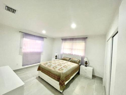 a white bedroom with a bed and two windows at Bright & Cozy Family Home Near Dania Beach in Dania Beach