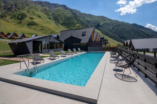 a swimming pool with chairs and mountains in the background at Kazbegi Targmani Cottages in Stepantsminda