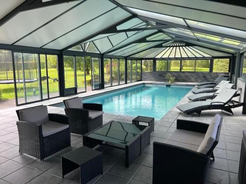 une grande piscine avec des chaises et un toit en verre dans l'établissement Villa Les Jardins de Parfondeval, à Parfondeval