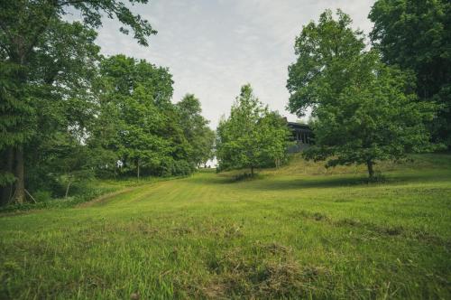 a field with trees and a house in the distance at Valmiera Riverside Retreat - Beverina Secret in Ķeiži