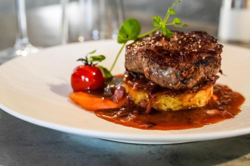 a plate of food with a piece of meat and a tomato at Logis Hôtel & Restaurant Le Cadet de Gascogne in Saint-Justin