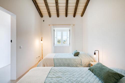 deux lits dans une chambre blanche avec une fenêtre dans l'établissement Casa Paraíso, à Ferreira do Alentejo