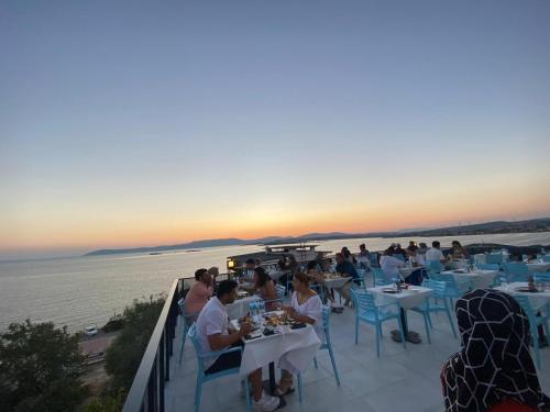 a group of people sitting at tables at a restaurant overlooking the water at Ugem in Seferihisar