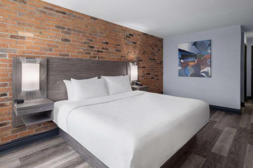 a bedroom with a white bed and a brick wall at Travelodge by Wyndham Barrie in Barrie