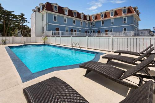 a swimming pool with two chairs and a building at Wildwood Inn Hotel Travelodge Beach & Boardwalk in Wildwood
