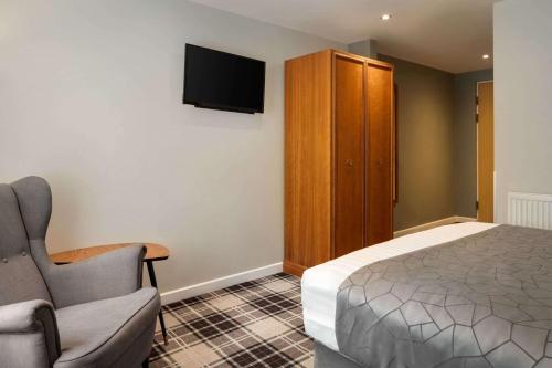 a bedroom with a bed and a chair and a cabinet at Heritage Park Pontypridd, Trademark Collection by Wyndham in Pontypridd